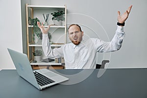 A man in a wheelchair businessman with tattoos in the office behind a laptop, anger and annoyance, hands up, the concept