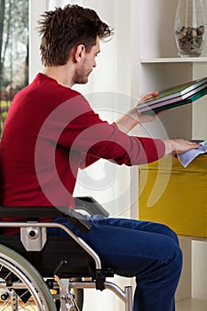 Man on wheelchair dusting shelves