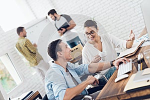 A man in a wheelchair is making a conversation with a girl. They are working in a bright office.