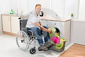 Man on wheelchair putting clothes into the washing machine