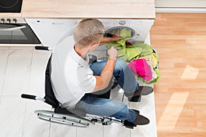 Man on wheelchair putting laundry into the washing machine