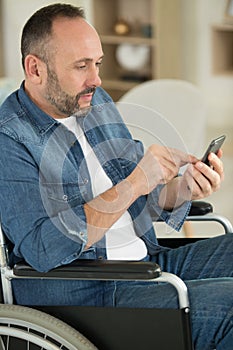 man on wheelchair talking by mobile phone in home office