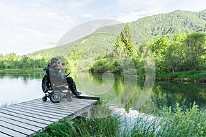 Man on wheelchair using mirrorless camera near the lake in nature