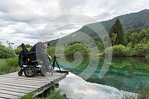 Man on wheelchair using mirrorless camera near the lake in nature