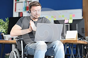 Man in wheelchair and wearing headphones with microphone works on laptop