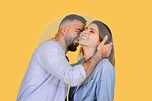 Man whispering to laughing woman on yellow backdrop