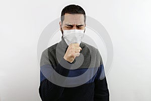 A man on  white background dressed in casual with protective medical mask coughs with his hand closed in front of his mout