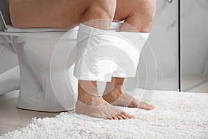 Man with white boxers sitting on toilet bowl in bathroom