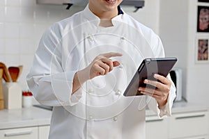 Man in white chef uniform holding and pointing digital tablet, using tablet for searching tasty meal recipes online internet, man