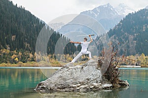 A man in white clothes with a sword stands on a large stone among the highlands