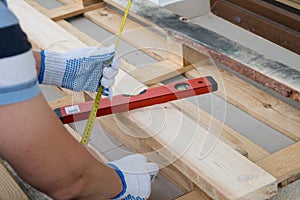 A man in white construction gloves measures a pine board with a tape measure