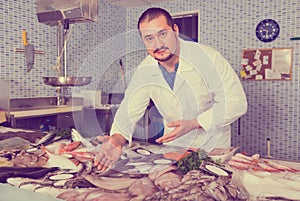 Man in white cover-slut showing fish on counter