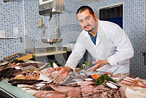 Man in white cover-slut showing fish on counter