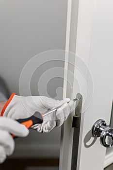 a man in white gloves holds a screwdriver and tightens the lock