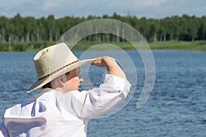 A man in a white hat looks into the distance on a river in the forest