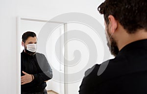 Man in white hospital home room look at mirror, wearing black shirt and white protective mask