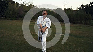A man in white kimono practicing kata karate early in the morning in the city park