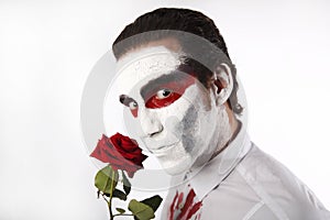 Man with white mascara and bloody shirt holds red rose