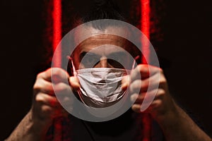Man with white medical mask standing in the dark, holding red bars made of viruses with his bare hands, locked away in dark