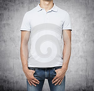 A man in a white polo shirt and denims holds his hands in pockets.