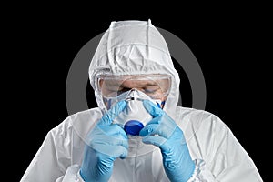Man in white protective suit and facepiece respirator, disposable blue gloves and goggles on black background