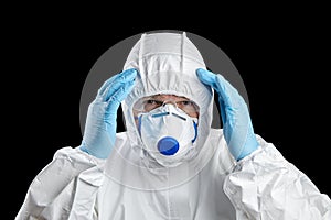 Man in white protective suit holds his head. Man in facepiece respirator and glasses, hands in disposable blue glove