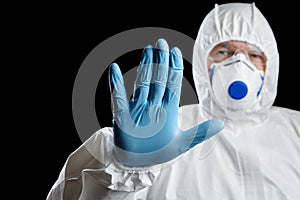 Man in white protective suit showing stop gesture on black background. Hand ind blue glove, palm stop sign