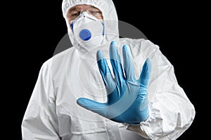 Man in white protective suit showing stop gesture on black background. Hand ind blue glove, palm stop sign