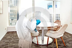 Man in a white protective suit spraying disinfectant in the office room photo