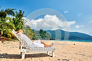 Man in white relaxing in sun bed on beach