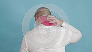 A man in a white shirt adjusts a red heating pad with hot water for pain in his neck. The concept of treatment of