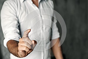 A man in a white shirt on a background of gray concrete pushes his index finger at the camera screen