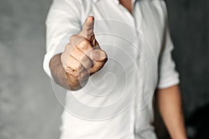 A man in a white shirt on a background of gray concrete pushes his index finger at the camera screen