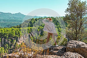 Man in white shirt and brown hat is standing on rock near cliff in front of the Grand Canyon around the forest beautiful amazing