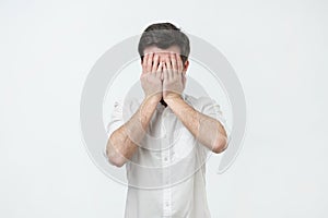 Man in white shirt covered his face with his hands