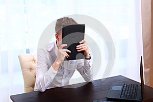 A man in a white shirt covered his face with a leather-bound book. Avoiding problems. The concept of a financial crisis