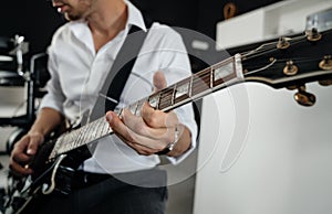 Man in a white shirt on a dark background, holds an electric guitar in his hands and tunes the sound of strings.