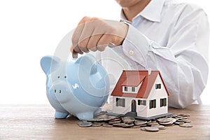 The man in the white shirt dropped the coin in the piggy bank next to the small house model