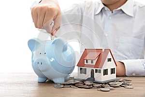 The man in the white shirt dropped the coin in the piggy bank next to the small house model