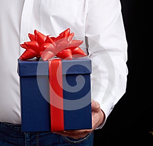 Man in a white shirt holds a blue gift cardboard box with a red bow