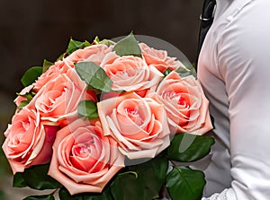 A man in a white shirt holds or hands a bouquet of salmon-colored roses.