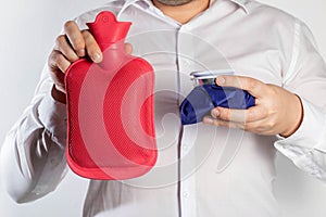 A man in a white shirt holds an ice bag and a red medical heating pad for hot water. The concept of heat and cold treatment. Close