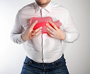 A man in a white shirt holds a red heating pad with hot water on his chest. Treatment of inflammation of the lungs and bronchitis photo