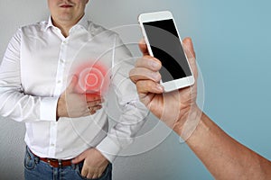 Man in a white shirt holds on to the chest in the region of the heart, next to his hand is holding a phone with black display, the