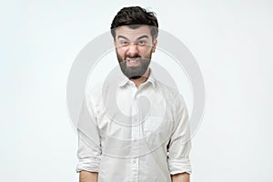 Man in white shirt isolated against white studio background. His face is in disgust grimace.