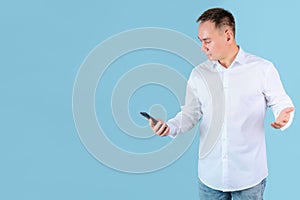 A man in a white shirt looks at the phone screen and irritably spreads his hands. Blue background, copyspace