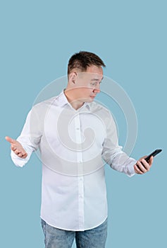 A man in a white shirt looks at the phone screen and irritably spreads his hands. Vertical photo