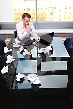 A man in a white shirt sits at a table and holds his head in his hands. A frustrated businessman. Headache. The concept