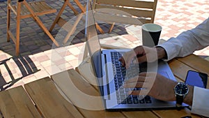 A man in a white shirt sits at a table in a street cafe, typing on a laptop keyboard. view from above. 4k. 4k video