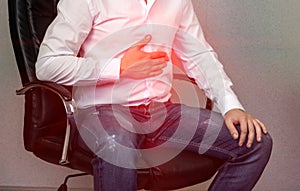 A man in a white shirt is sitting on a chair and holding on to the stomach, abdominal pain, heartburn